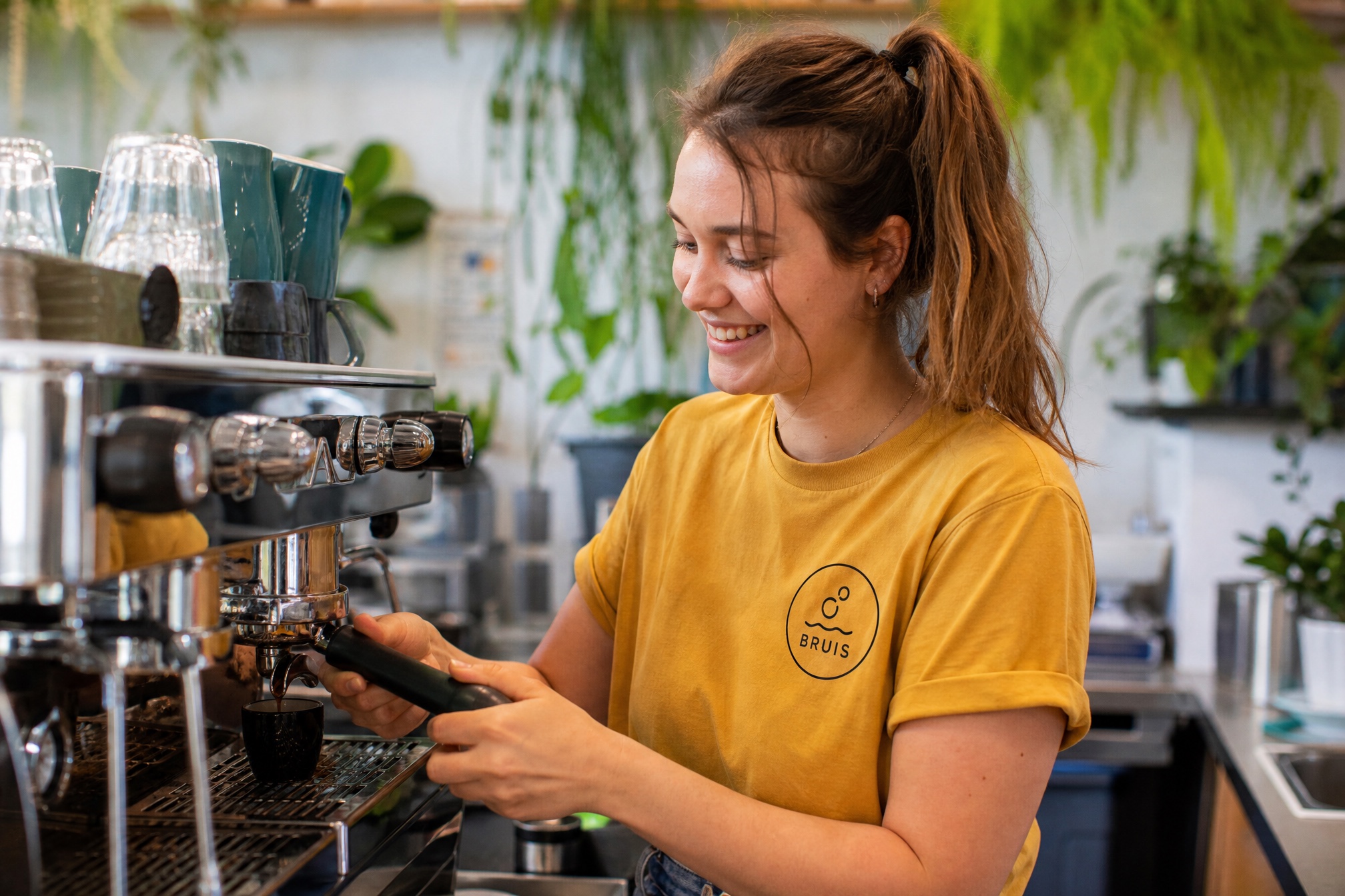 Barista van Bruis trekt een shot, het bubbel-logo op haar gele t-shirt