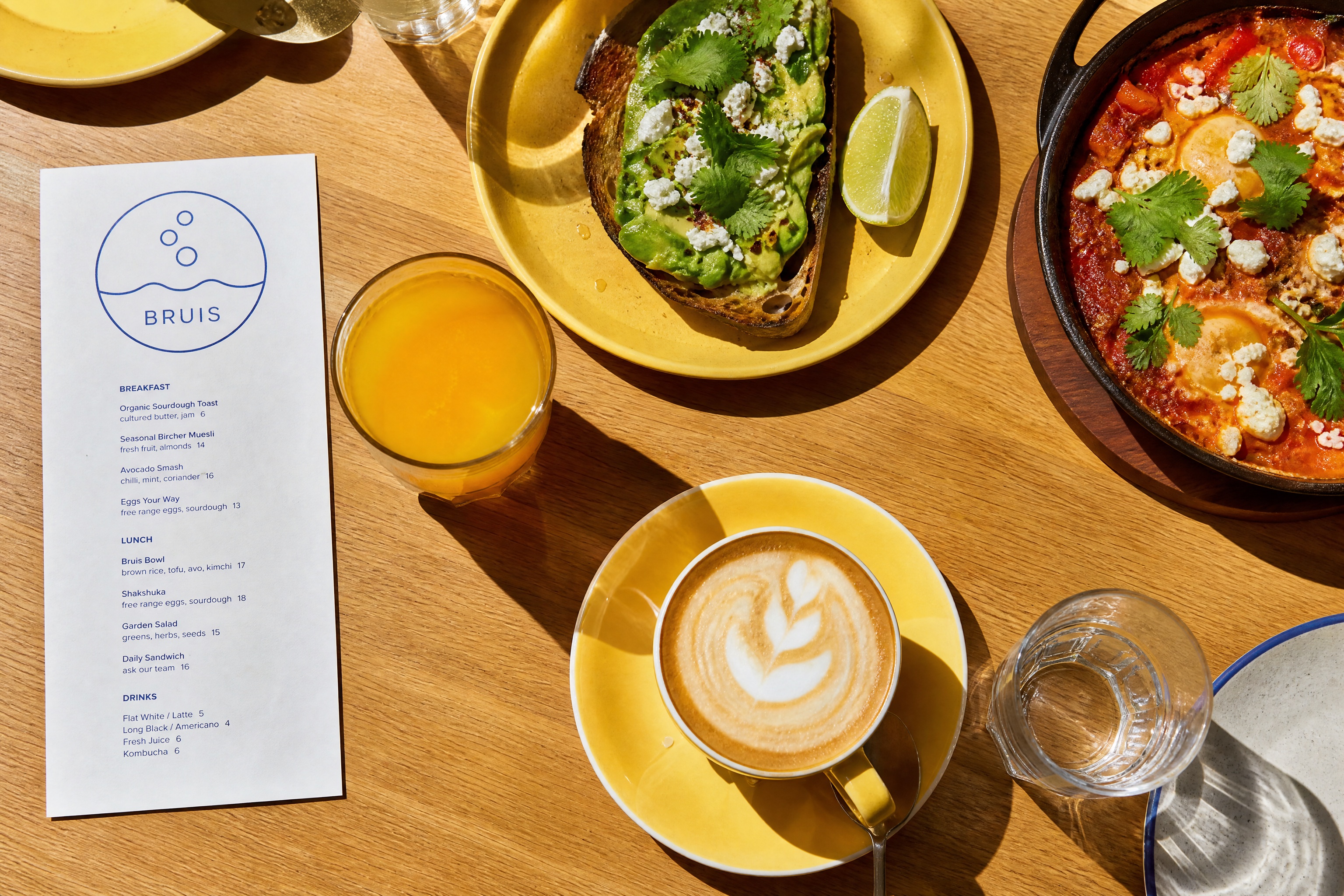 Brunchtafel van boven met avo-toast, shakshuka en verse jus, menukaartje met bubbel-logo