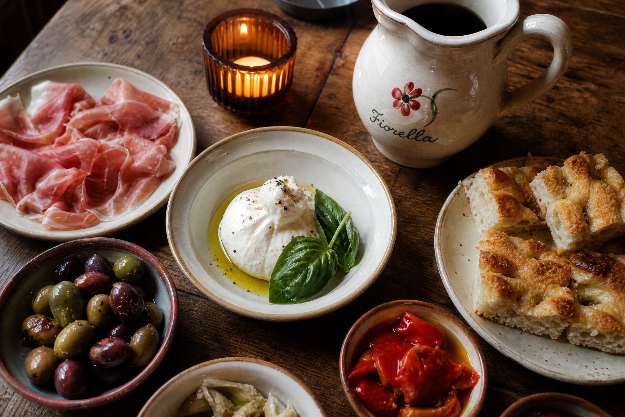 Antipasti-flatlay met burrata en focaccia, de wijnkaraf draagt de handgeschilderde bloem