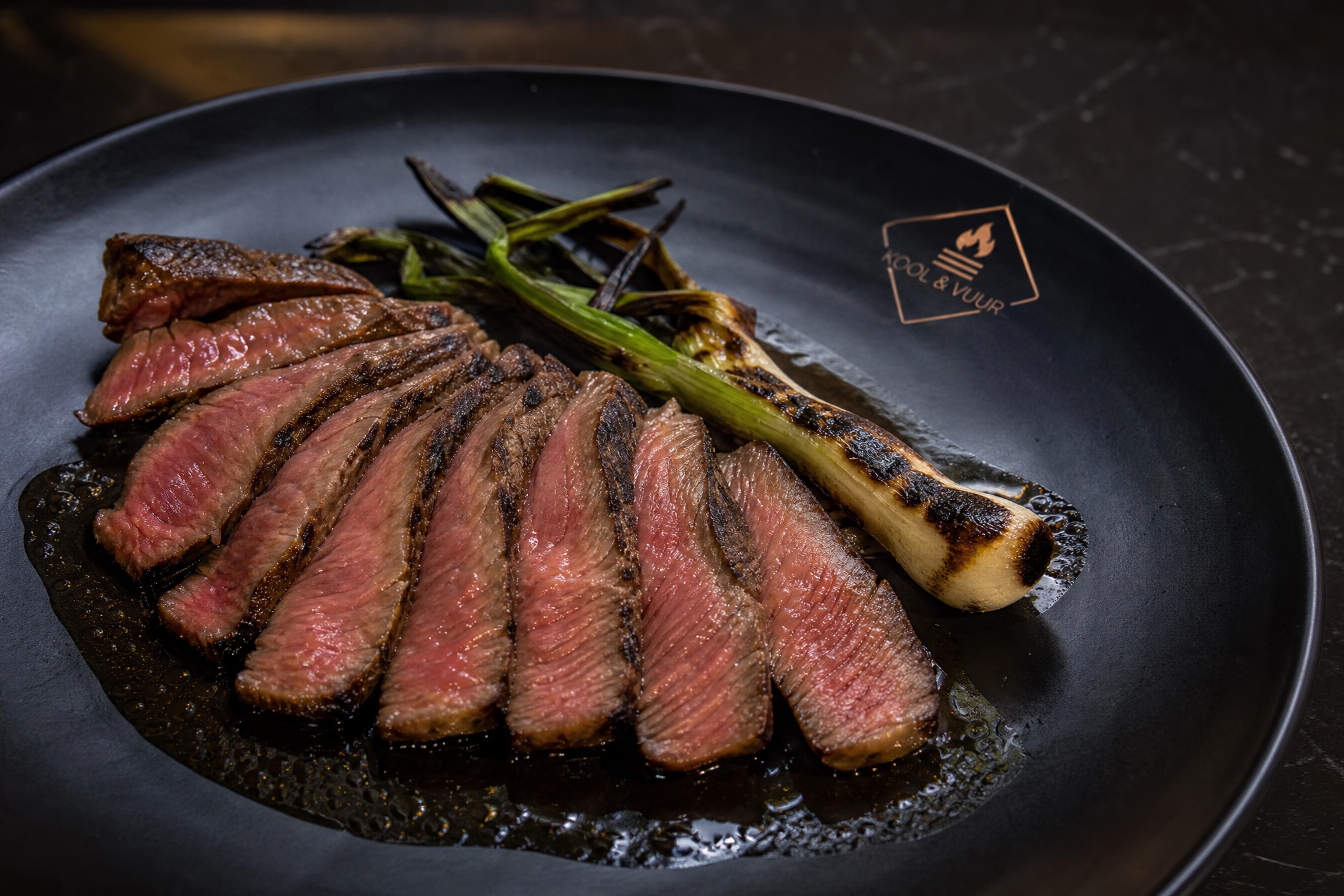 Getrancheerde steak op mat zwart keramiek met koperen embleem-stempel