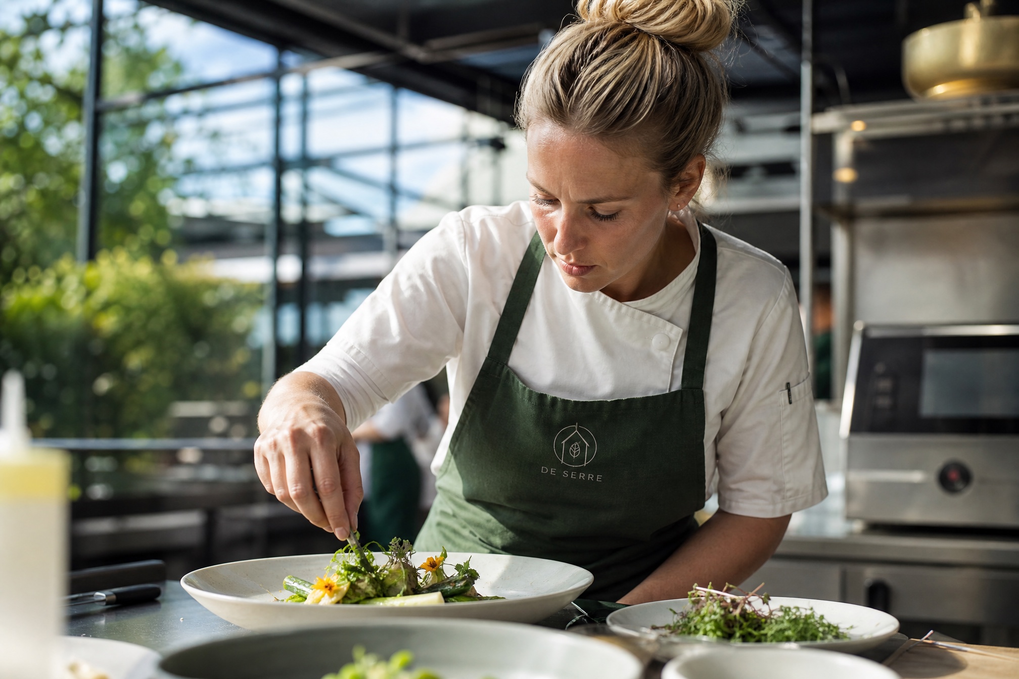 Chef De Serre plateert een groentegerecht, het serre-monogram geborduurd op haar groene schort